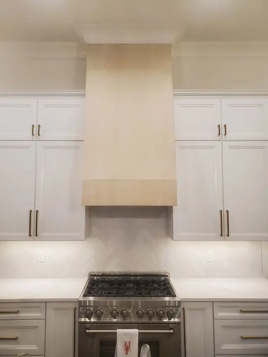 Flat-panel wood kitchen range hood over a herringbone tile backsplash
