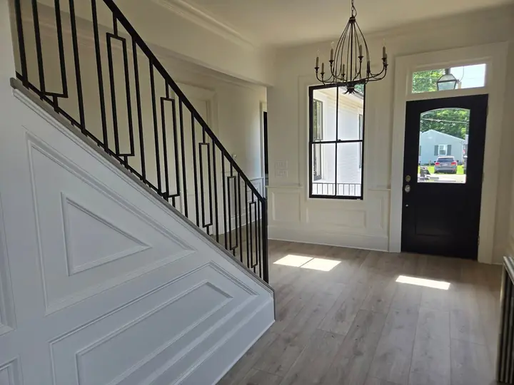 Entry foyer staircase with raised wall paneling and black iron railing