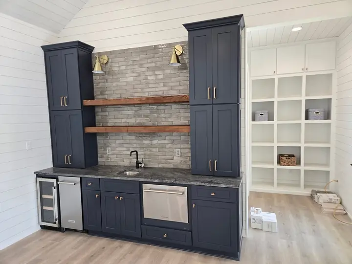 Navy blue built-in wet bar with brass hardware, floating wood shelves and tile backsplash