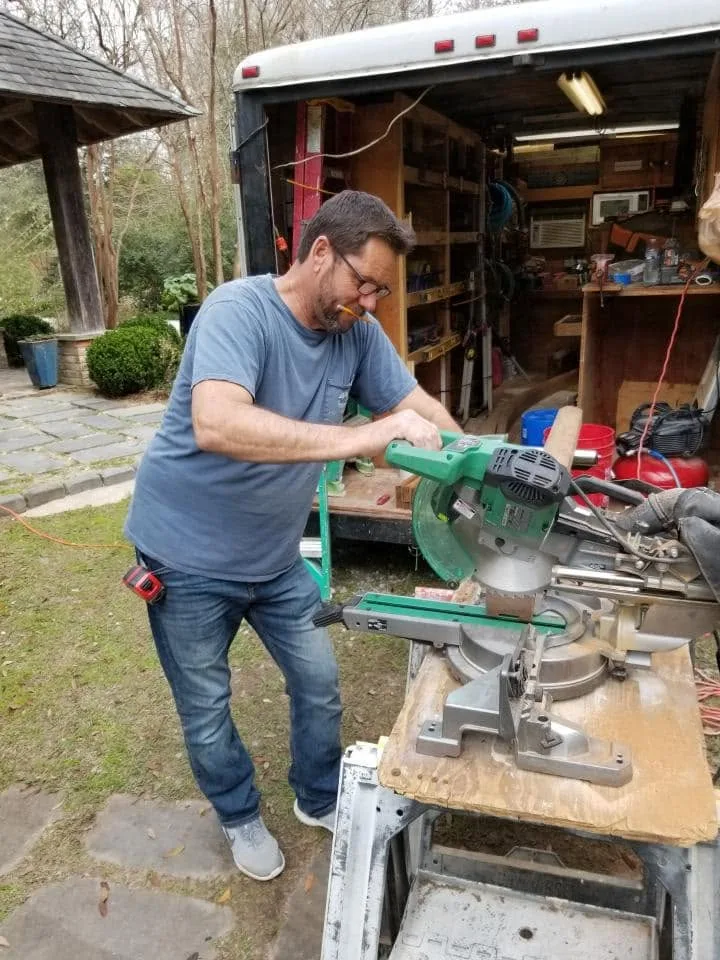 Craftsman cutting trim at a miter saw outside a work truck